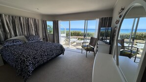 Quarto com cama grande, televisão e varanda com vista para o mar.