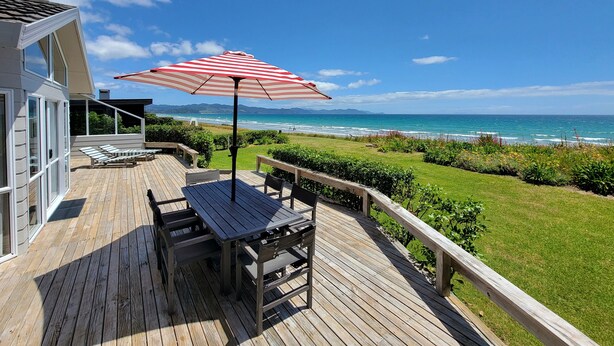 Um deck de madeira com mesa e cadeiras, um guarda-sol listrado e vista para o oceano.