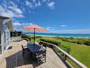 A wooden deck with a table and chairs, a striped umbrella, and a view of the ocean.