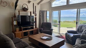 Sala de estar com televisão, mobiliário de madeira, vista para o mar e varanda.