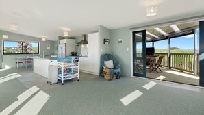 A spacious living area with a kitchen, dining area, and a balcony with a view. - The Blue Cottage with WiFi- Waipu Holiday Home (Waipu Cove)