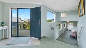 A modern interior with a sliding glass door leading to a balcony, a small bedroom with a bed and bedside table, and a hallway with a door leading to another room. - The Blue Cottage with WiFi- Waipu Holiday Home (Waipu Cove)