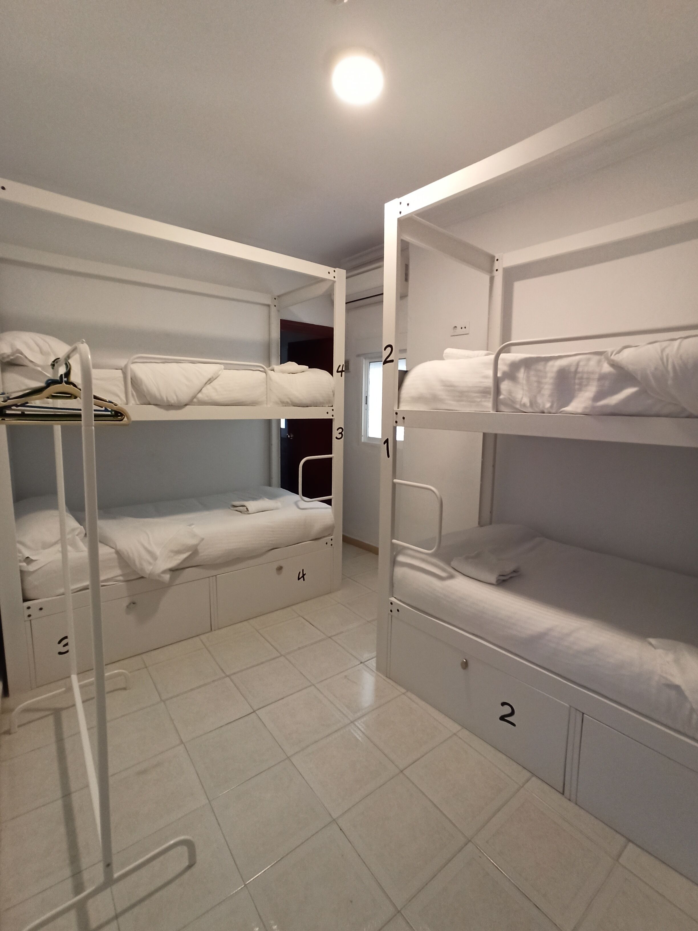 Un dormitorio con literas dobles, una escalera metálica blanca y piso de baldosas.