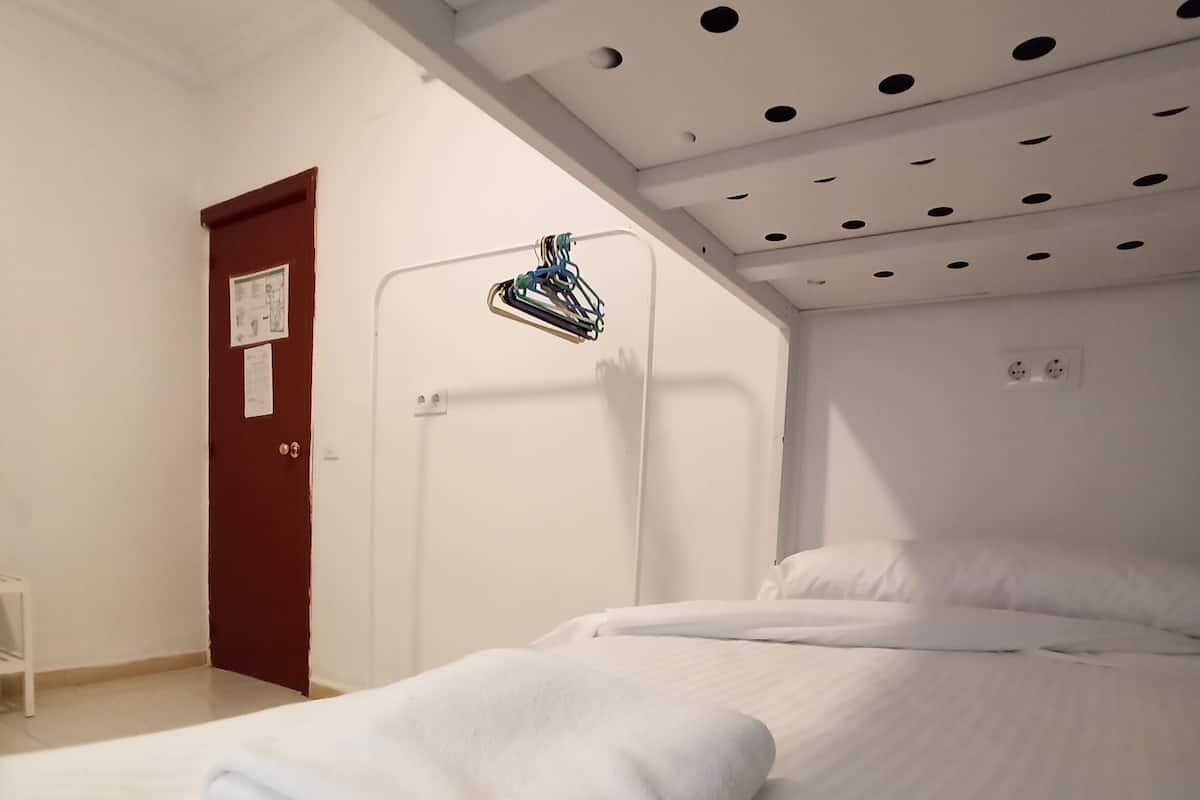 Una habitación de hotel con una cama bien hecha, una puerta roja y un techo con lámparas circulares.