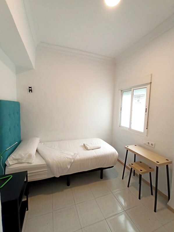 A small, clean room with a bed, a desk, and a window.