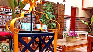 A traditional Moroccan-style room with a wooden table and chairs, a decorative metal stand, and a patterned wall. - Vivian's Guest House Auto Check-in (Jerez de la Frontera)