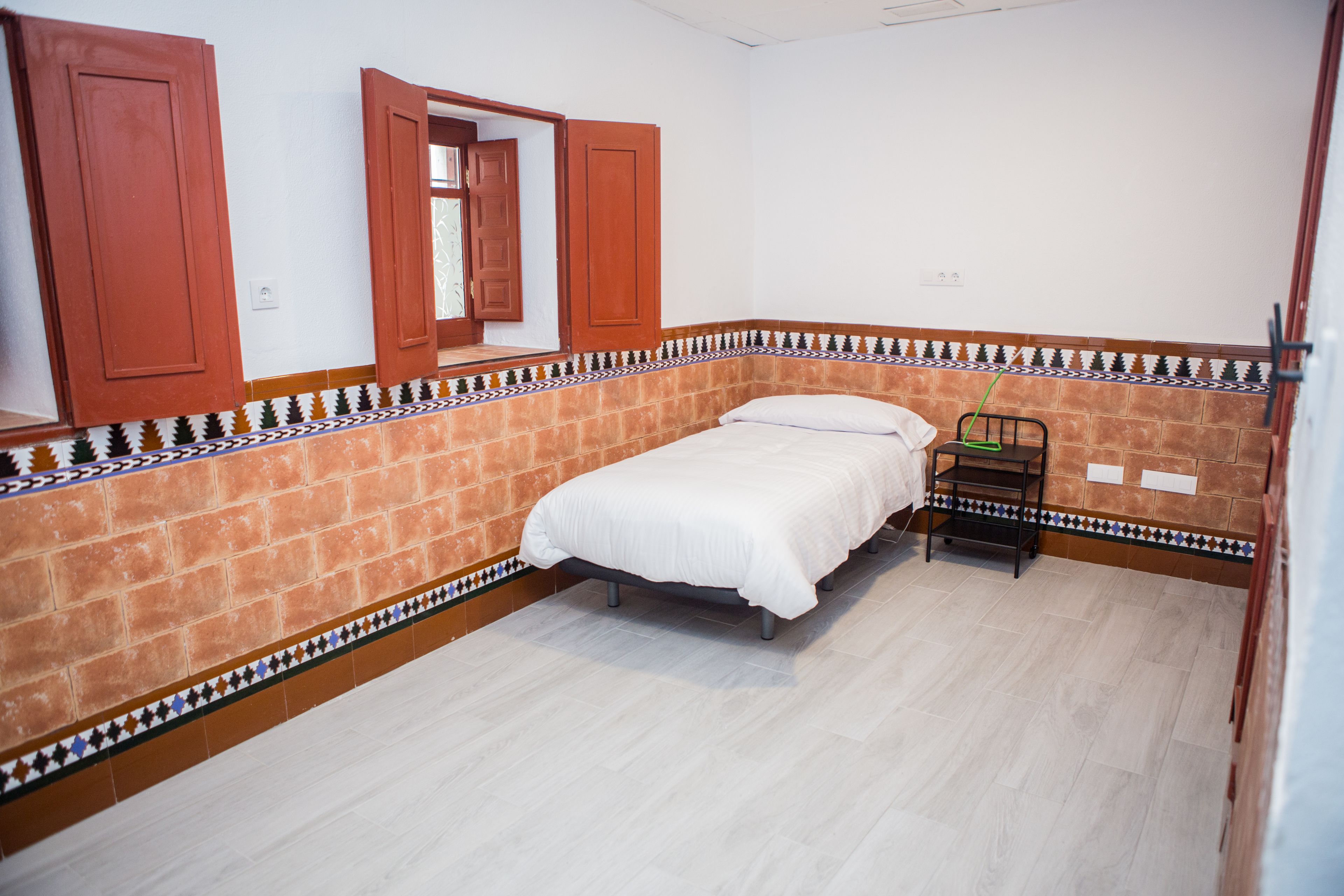 A bedroom with a bed, a nightstand, and a window with open shutters.