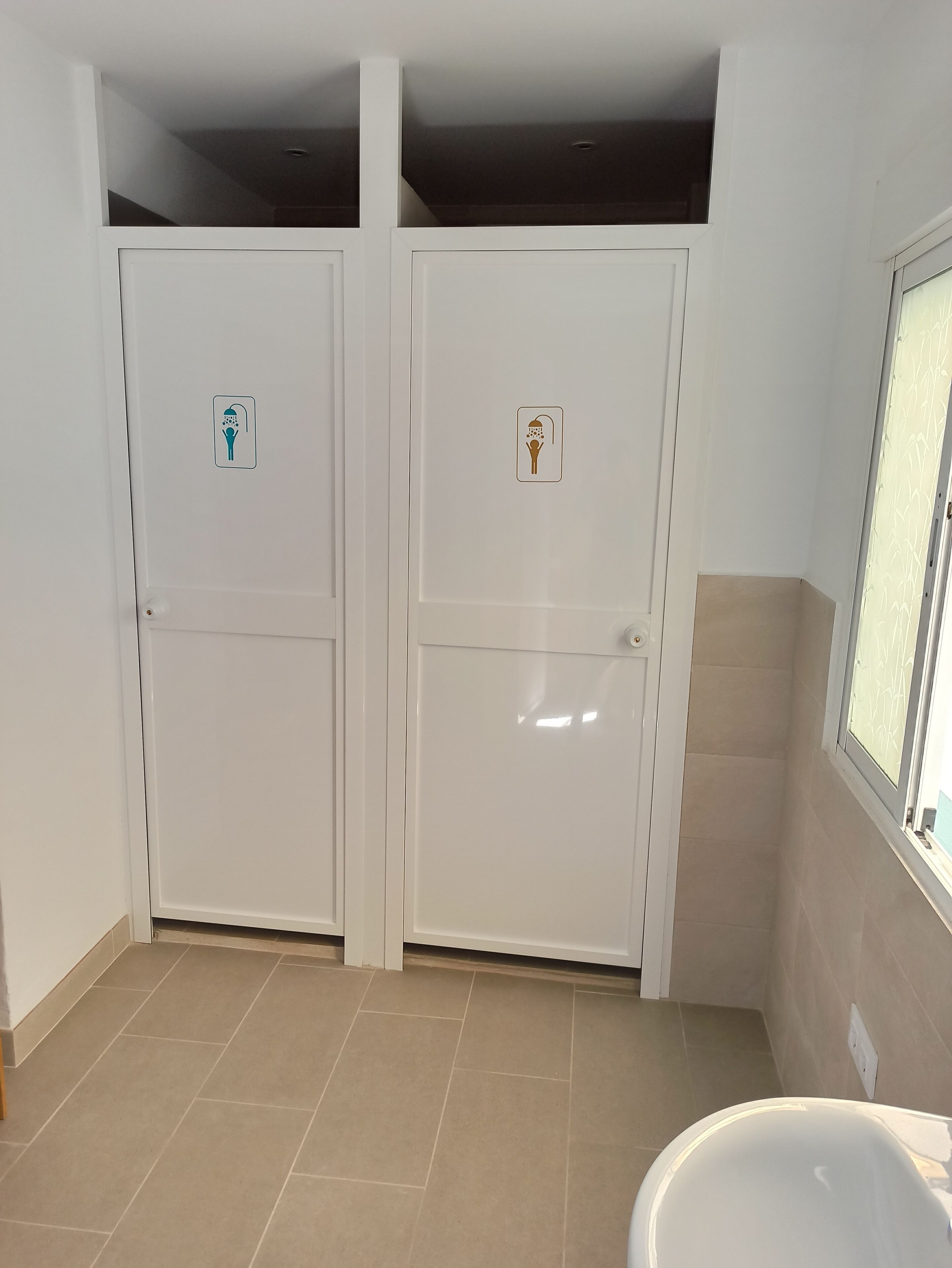 Un baño con dos puertas blancas, una con un icono de ducha y la otra con un icono de inodoro.