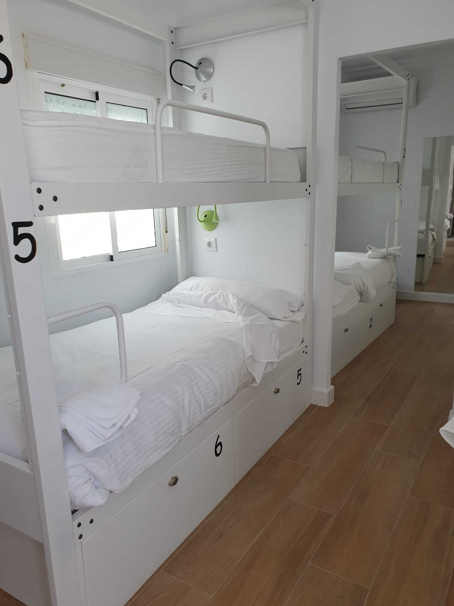 A bunk bed room with white bedding and a green wall-mounted light fixture.