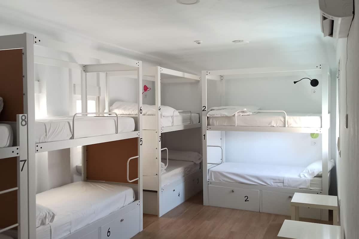 Un dormitorio con literas, una mesita pequeña y un aire acondicionado instalado en el techo.