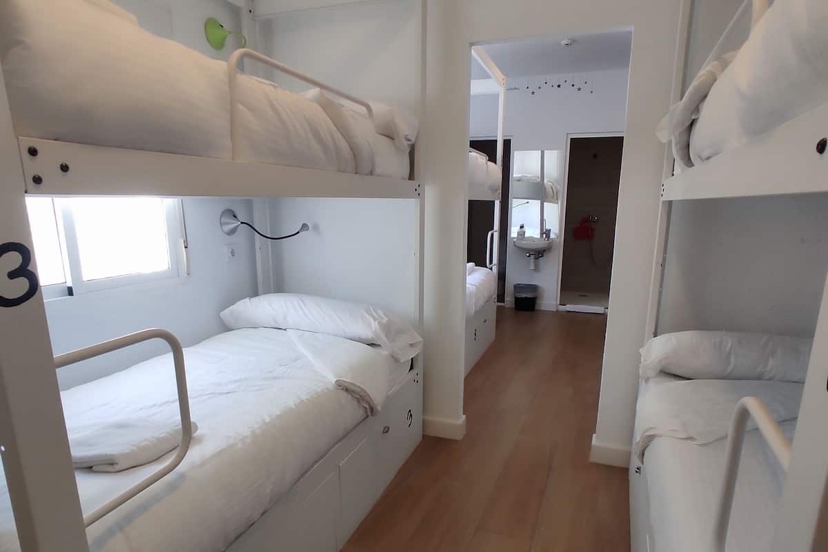 Un dormitorio con literas, una ventana, un lavamanos y una puerta que da a otra habitación.