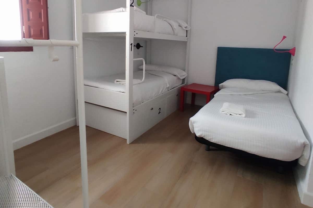Un dormitorio con literas, una mesita pequeña y una cama con cabecera.