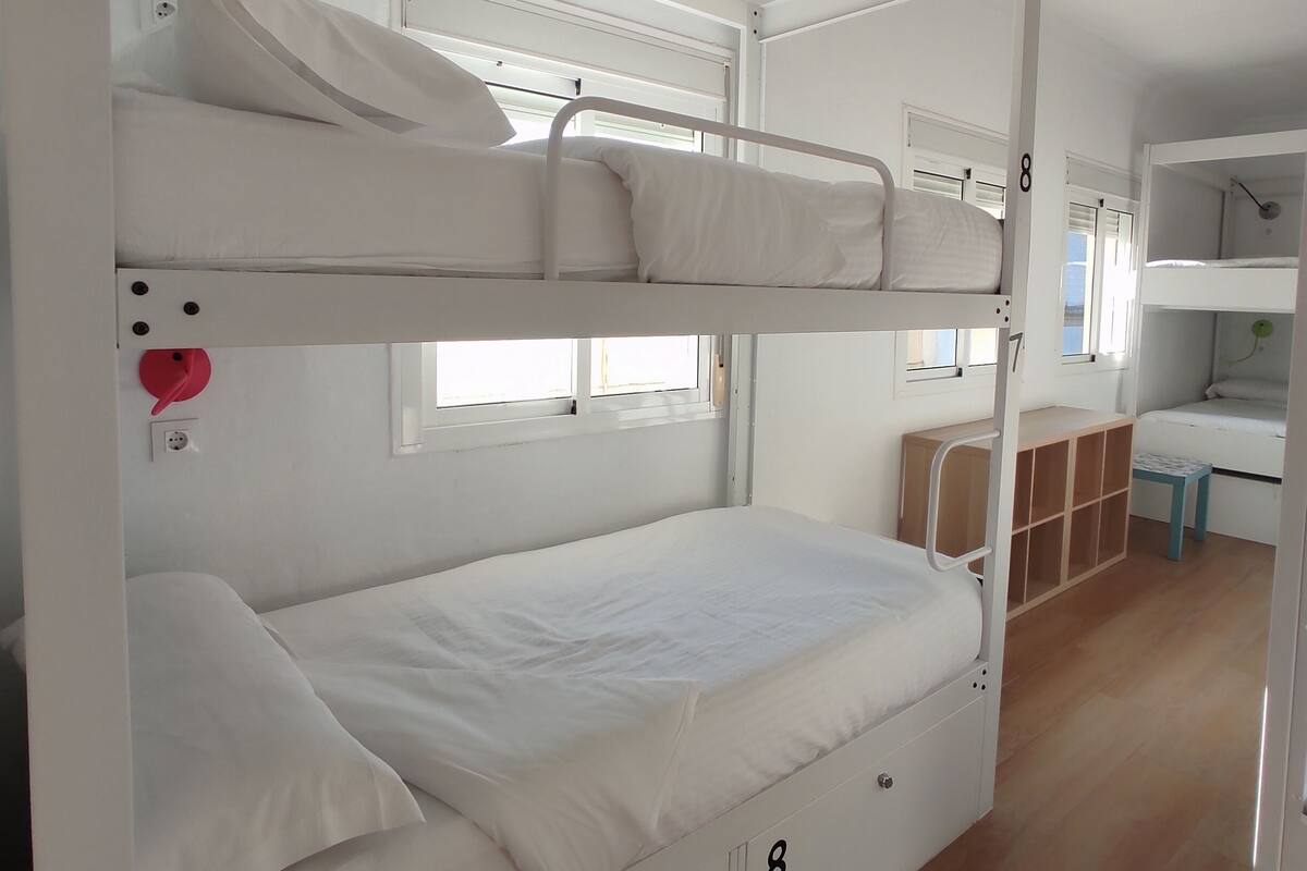 Habitación con literas, escritorio y estanterías, número 8, con buena iluminación y suelo de madera.