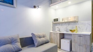 Uma kitchenette moderna com um sofá cinzento, um micro-ondas e um frigorífico pequeno.