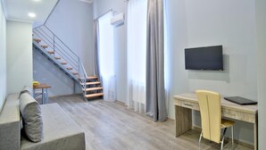 Uma sala de estar moderna com escada, televisão de tela plana, escrivaninha e sofá.