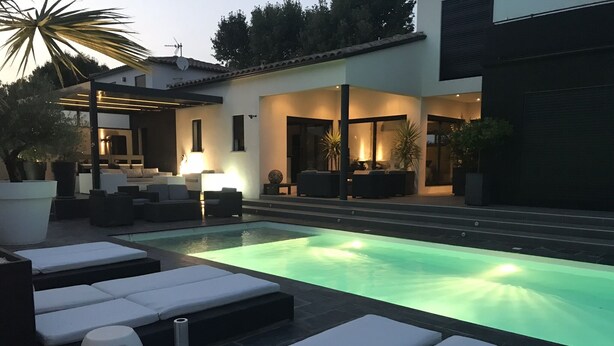 Un área de piscina moderna al aire libre con sillones de descanso y un patio bien iluminado.