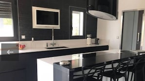 Una cocina moderna con una isla grande, taburetes negros tipo bar y un televisor integrado.