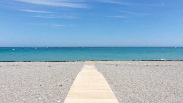 Ein Strand mit einer Holzstege, der zum Wasser führt.