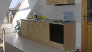 A kitchen with wooden cabinets, a coffee maker, a sink, and a window. - Wohnung Segelhafenidyll (Karlshagen)
