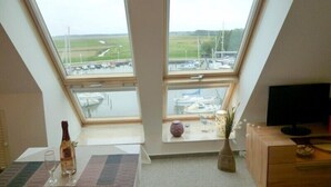 A room with a sloped ceiling and two large windows offering views of a marina and boats. - Wohnung Segelhafenidyll (Karlshagen)
