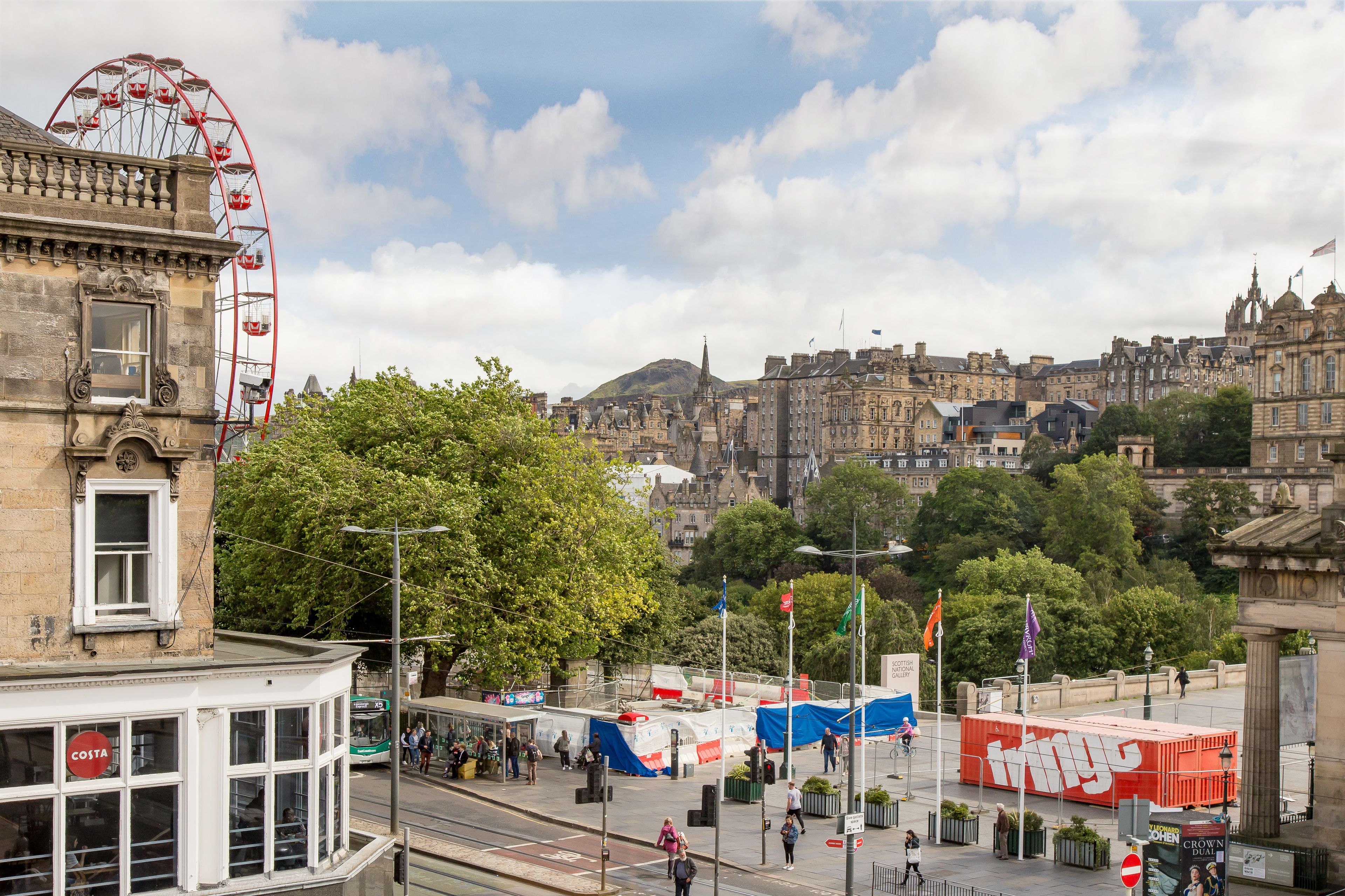 A historic building with a Ferris wheel in the background, a busy street with pedestrians, and a large red container labeled "things" in the foreground.