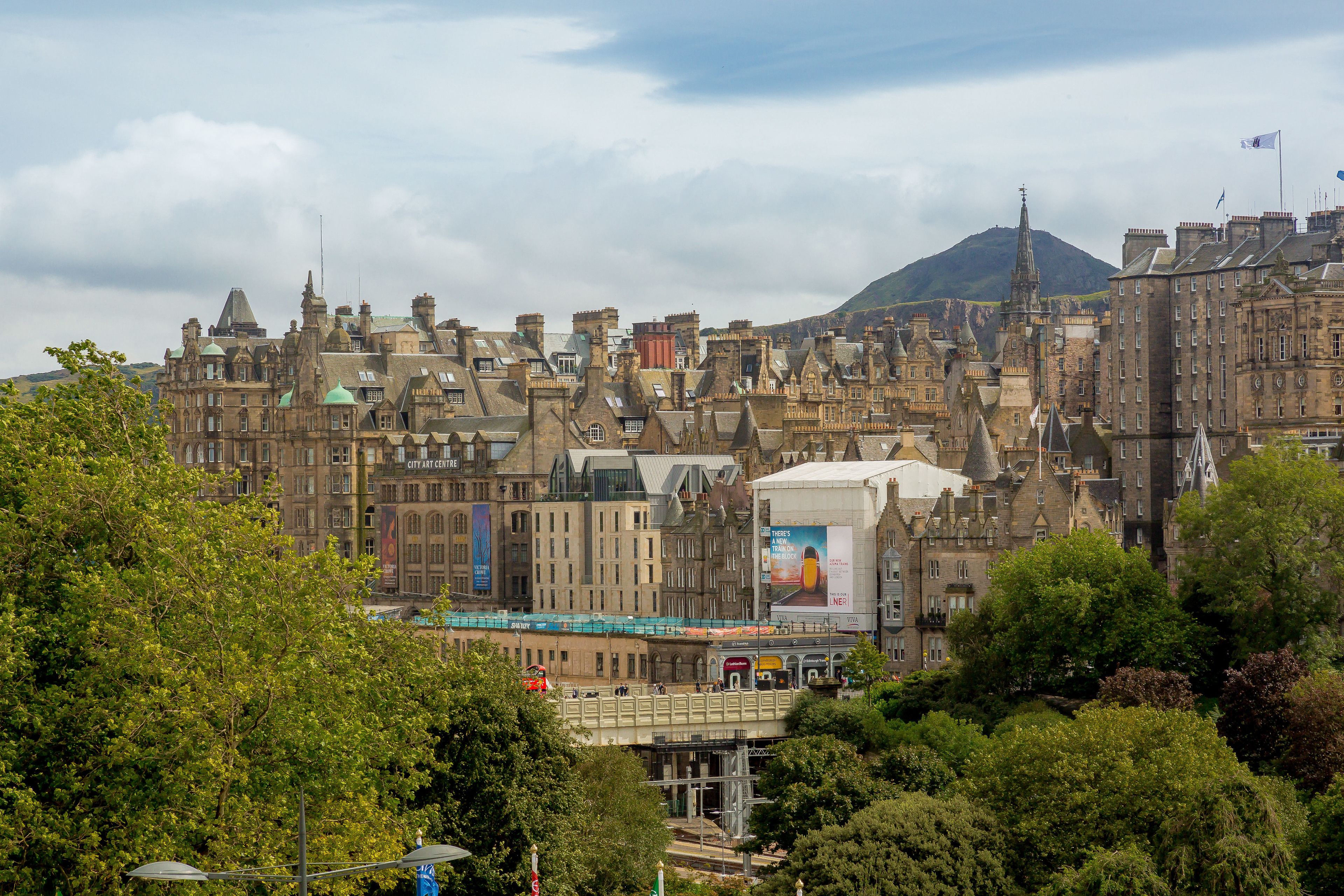 A historic cityscape with traditional architecture, a prominent building with a large billboard, and a bridge over a river.