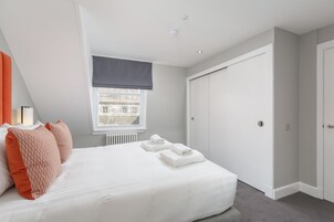 A bedroom with a bed, two pillows, a window with a view, a radiator, and a door.