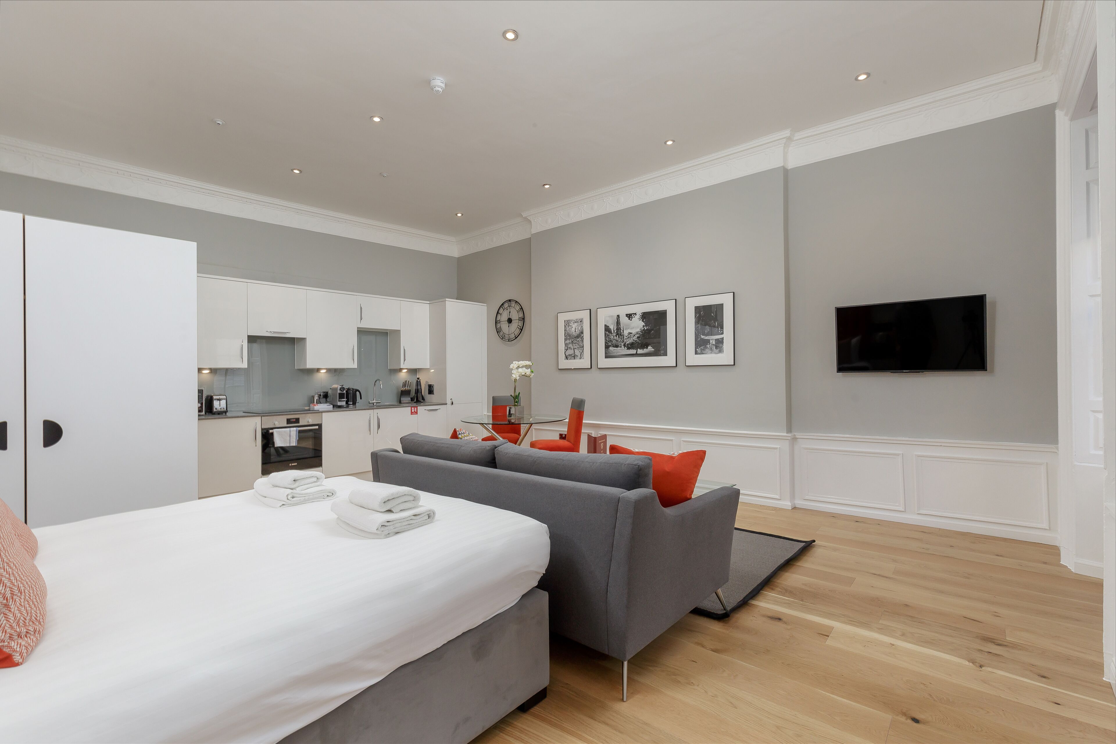 A modern hotel room with a bed, grey sofa, and a TV.