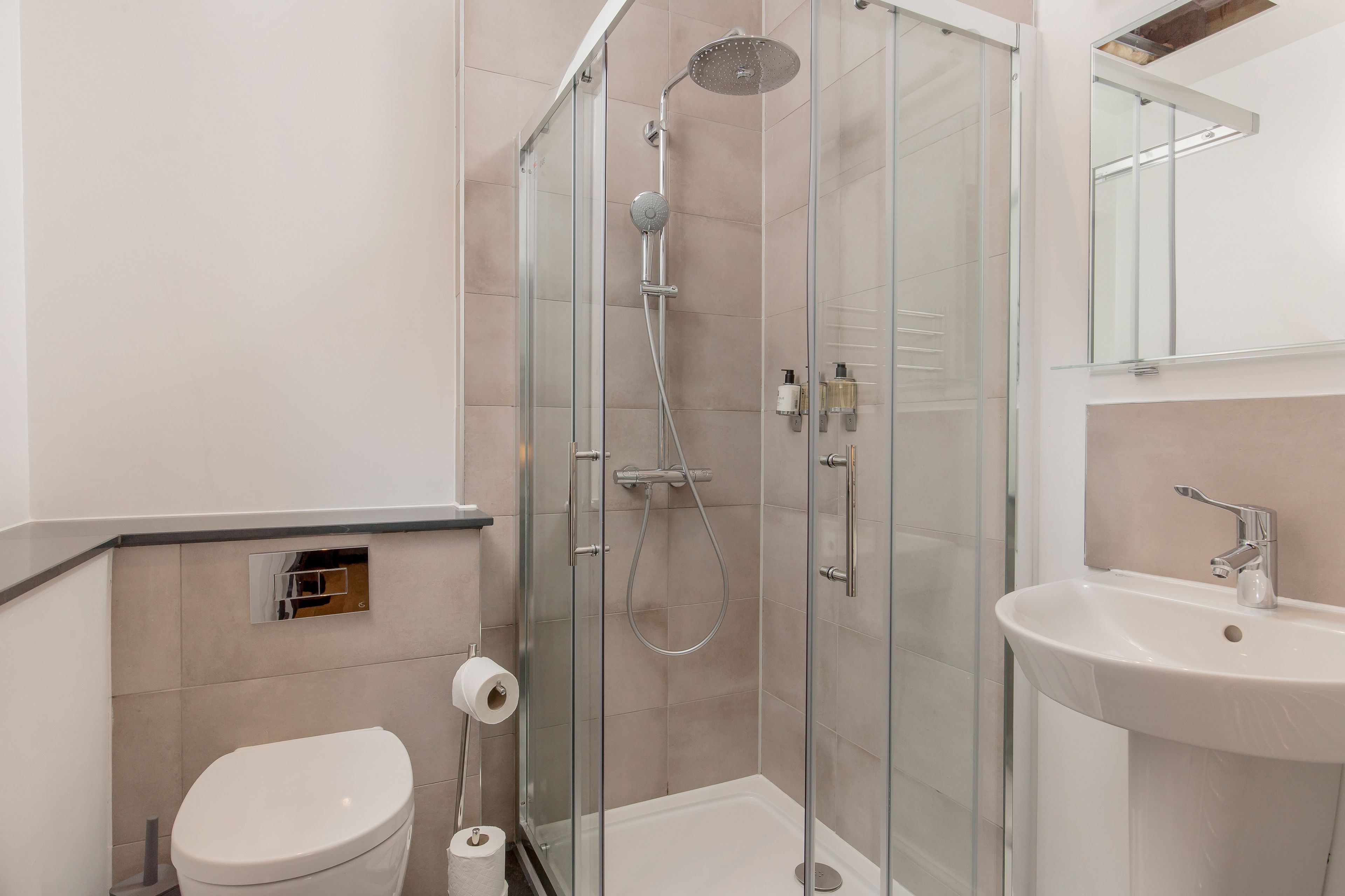 A modern bathroom with a glass-enclosed shower, a white toilet, and a sink with a mirror above it.