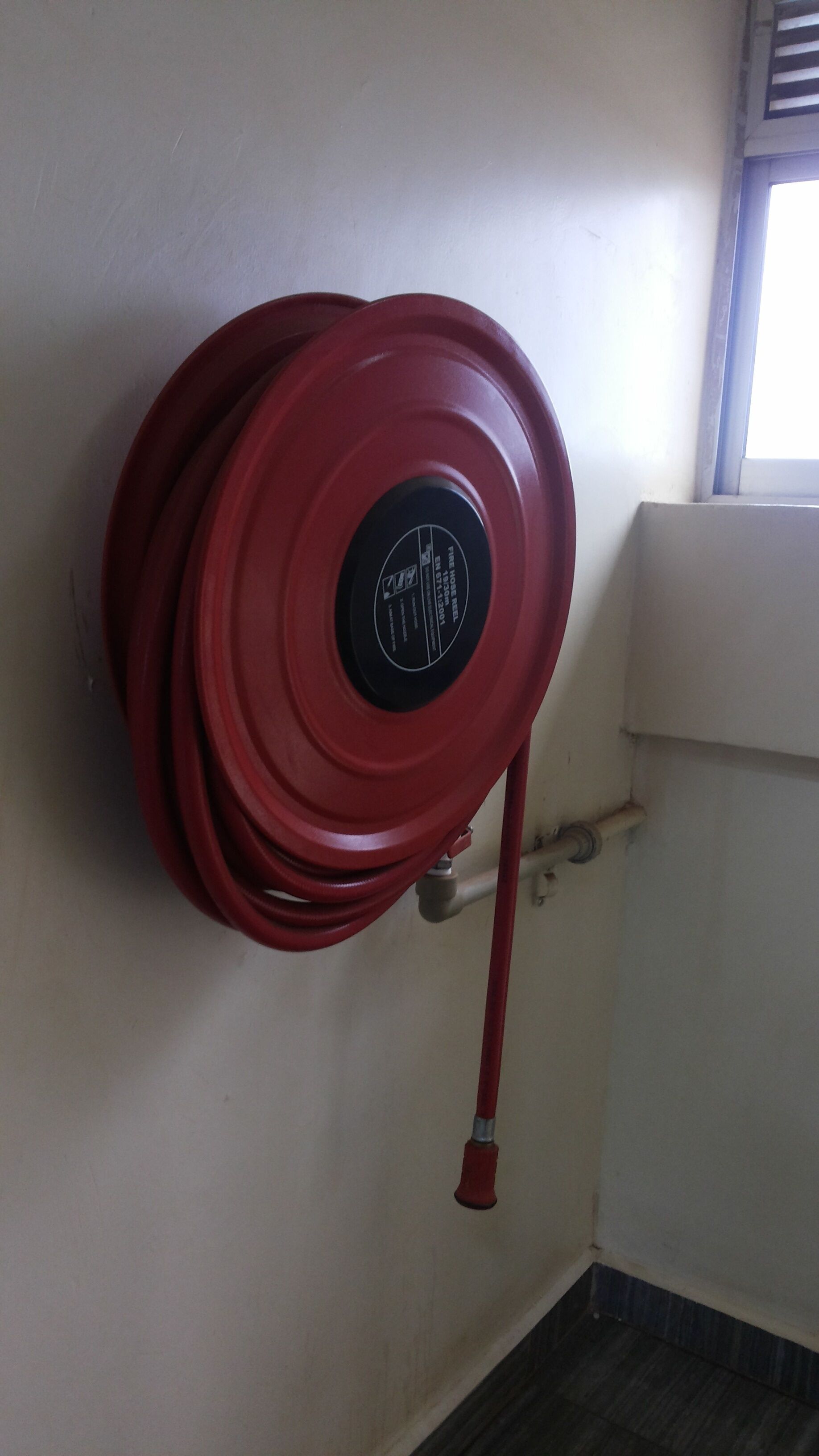 A red fire hose coiled against a wall with a window in the background.