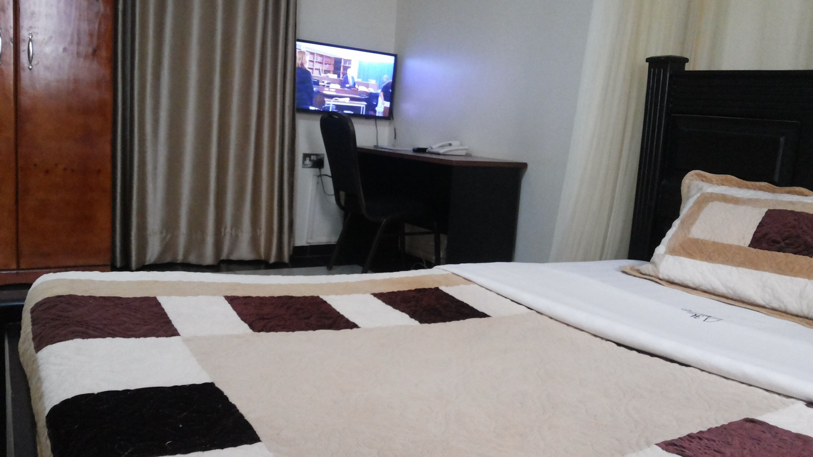 A hotel room with a bed, a desk with a chair, a television, and curtains.