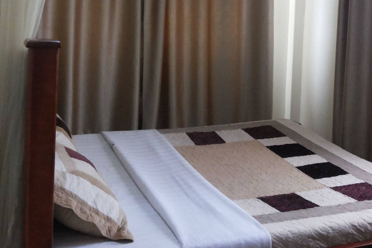 A single bed with a white mattress and a patterned blanket, a wooden headboard, and a canopy with sheer white fabric.