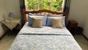 A bed with a floral-patterned bedspread, a wooden headboard, and several pillows. - Tropical Garden Self Catering (Mahé Island)