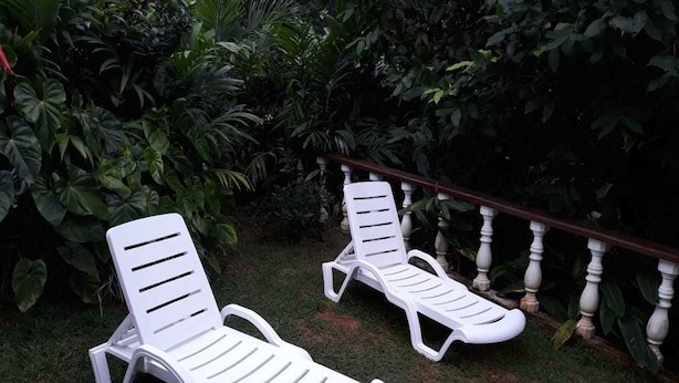 Two white plastic lounge chairs in a garden with a wooden balustrade and lush greenery. - Tropical Garden Self Catering (Mahé Island)