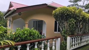 A two-story house with a red roof, beige walls, and a white balcony railing. - Tropical Garden Self Catering (Mahé Island)