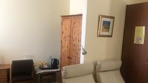 Una habitación con dos sillones color beige, un escritorio de madera con lámpara, un cuadro en la pared y un armario de madera.