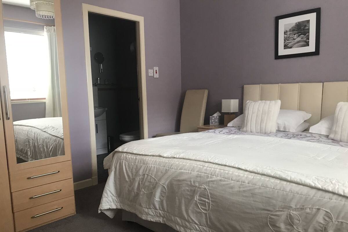 A bedroom with a large bed, a wardrobe, a mirror, and a framed picture on the wall.