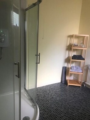 A bathroom with a glass shower door, a metal handle, a towel rack with towels, and a black textured floor. - Amalfi Bed & Breakfast (Dornoch)