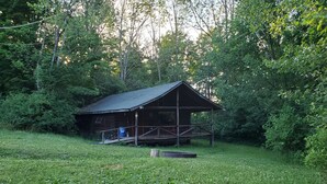 Een rustieke houten hut met een veranda, omringd door weelderige begroeiing.