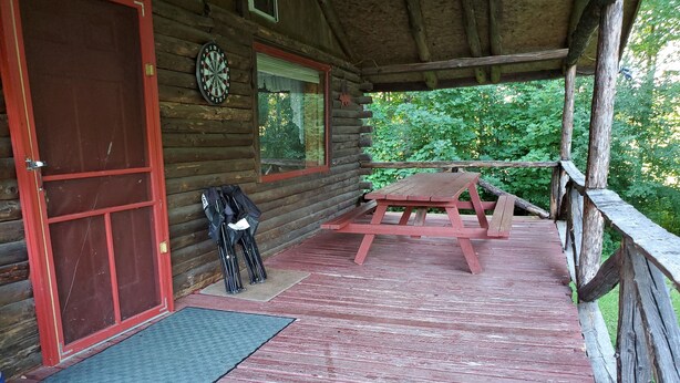 Een houten vakantiehuisje met een rode deur, een dartbord en een picknicktafel op het terras.