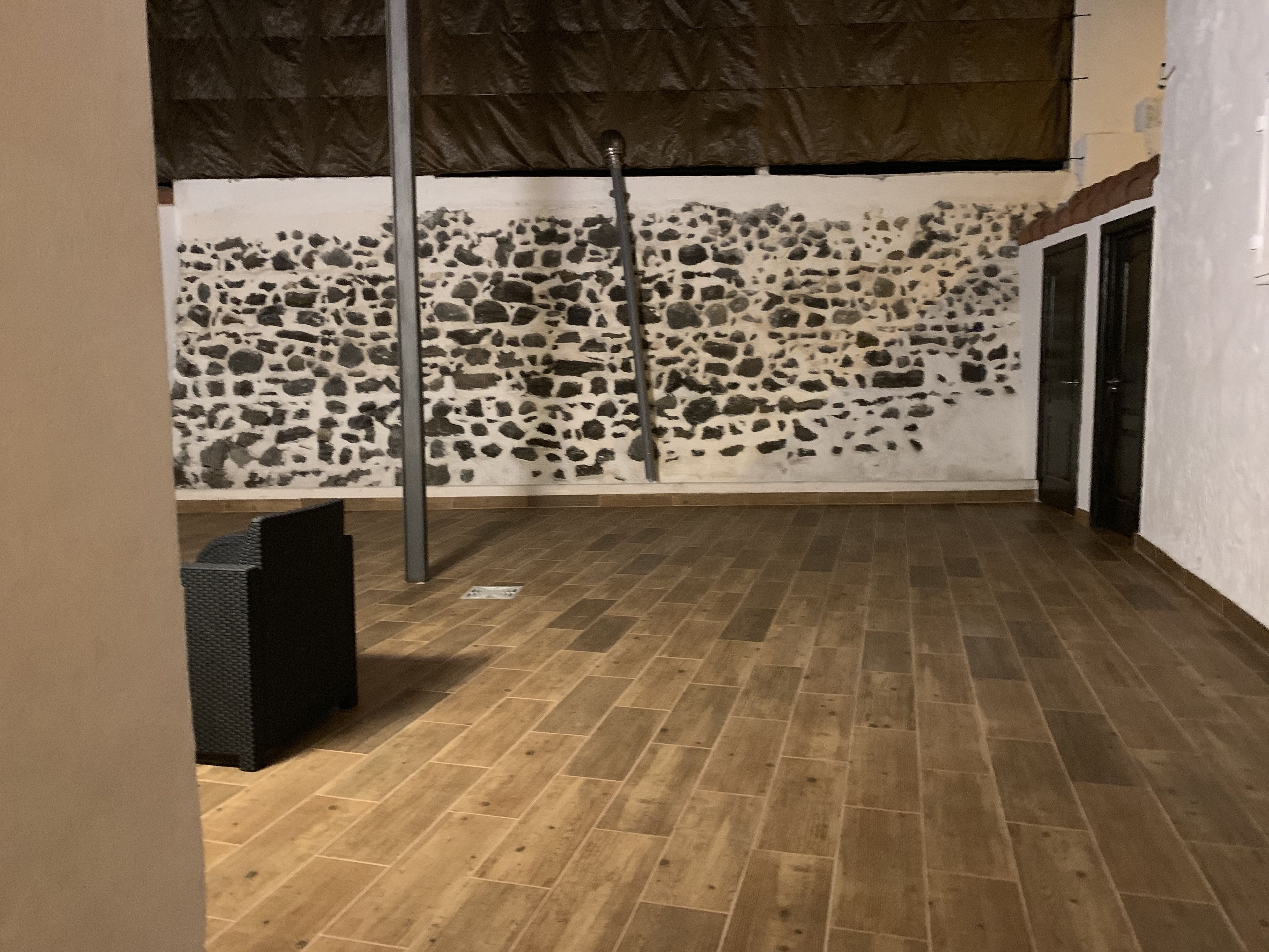A room with a stone wall, a wooden floor, and a metal pole.