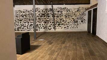 A room with a stone wall, a wooden floor, and a metal pole.