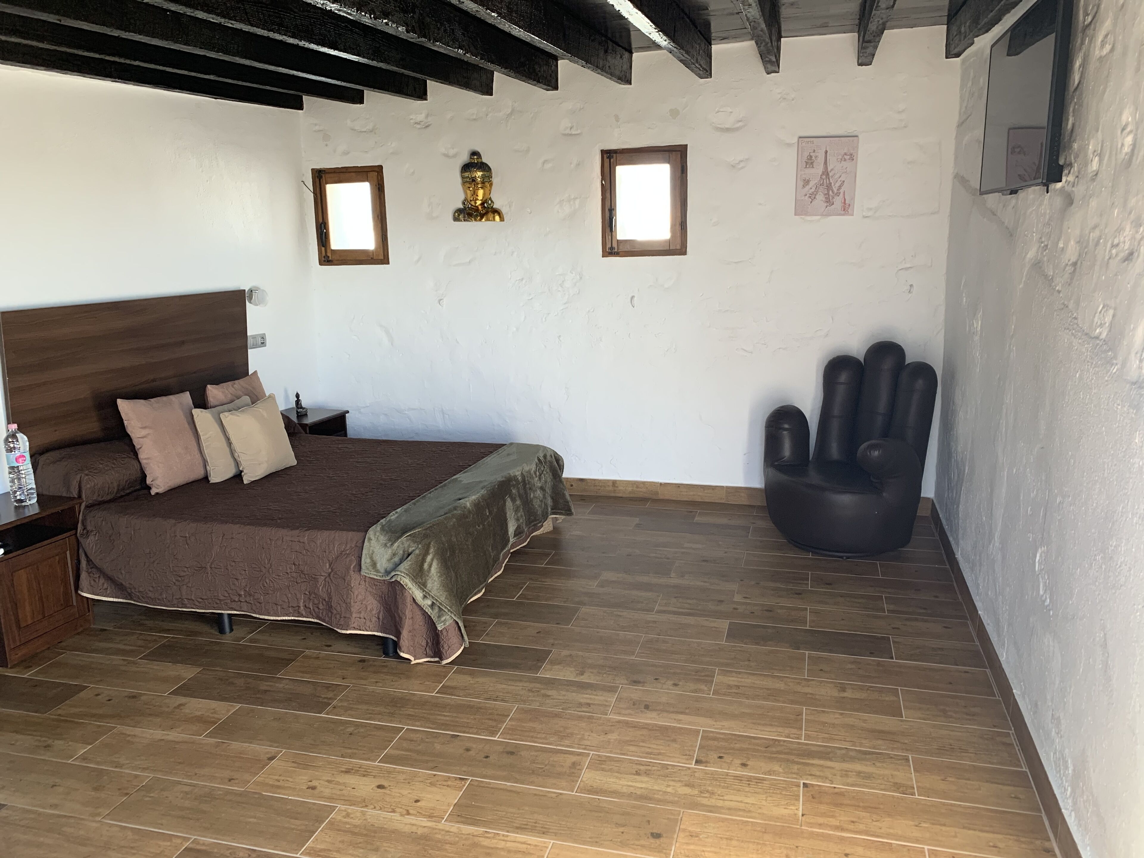 A bedroom with a wooden bed, a nightstand, a black chair, and a small window.
