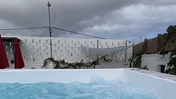 A swimming pool with water splashing, surrounded by buildings and a cloudy sky. - Valtisya House Pool & Airport (Telde)