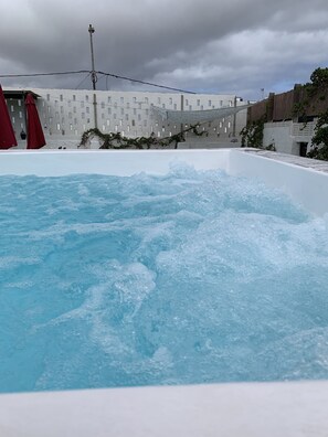 A swimming pool with water splashing, surrounded by buildings and a cloudy sky. - Valtisya House Pool & Airport (Telde)