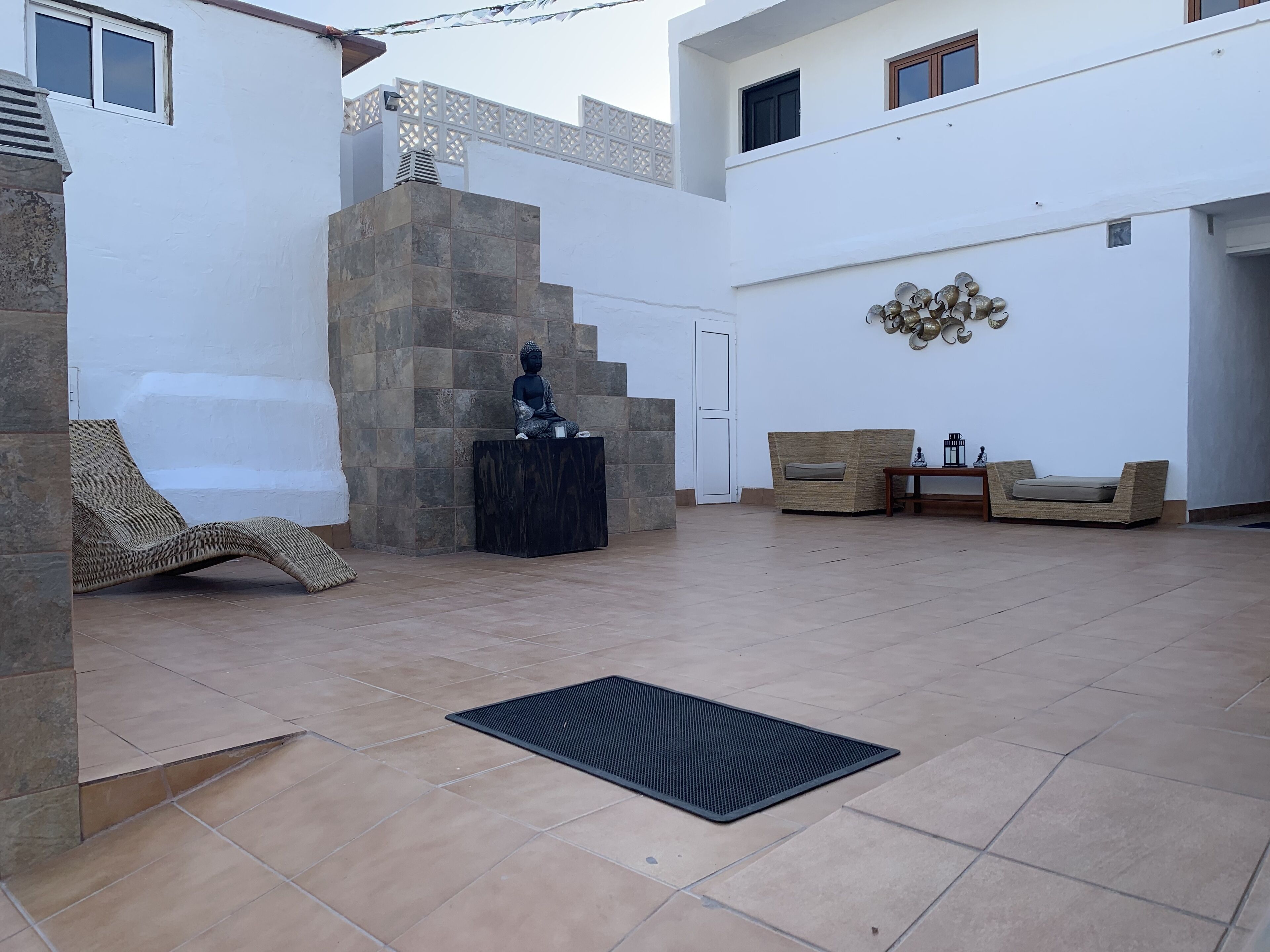 Un amplio espacio al aire libre con una estatua de piedra, una silla lounge de mimbre, un sofá acolchado y un elemento decorativo en la pared.
