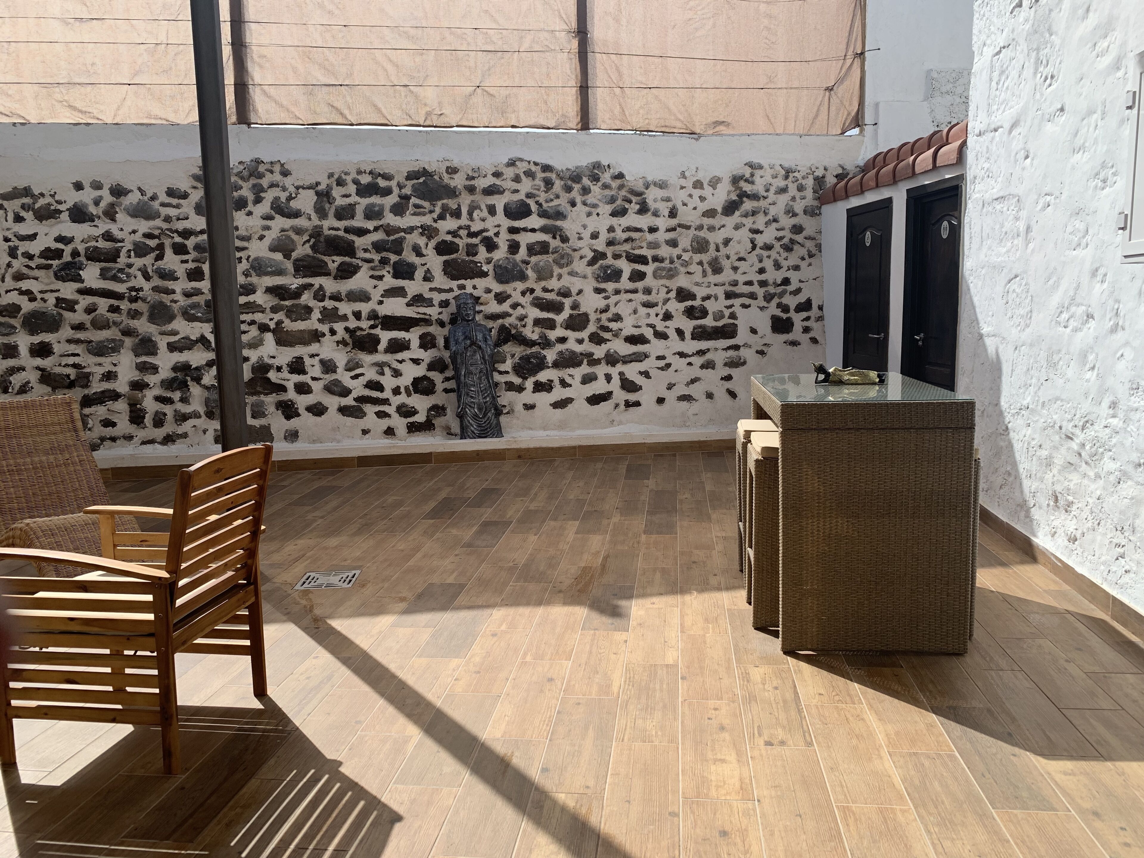 Un patio con muros de piedra, una estatua, mobiliario de mimbre y piso de baldosas.