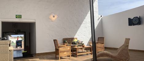 A sunlit patio with a table and chairs, a wicker chair, and a dartboard on the wall.