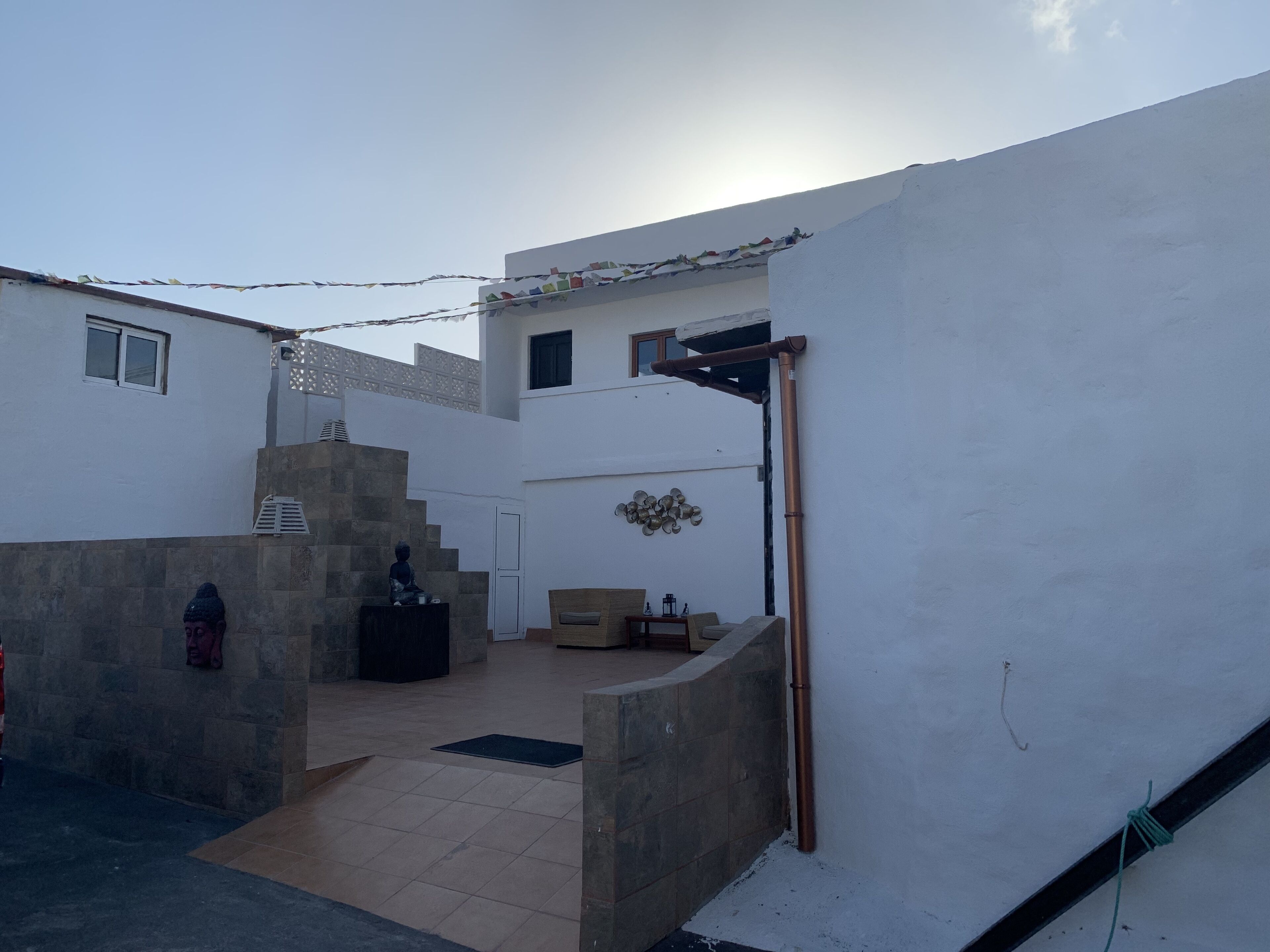 A courtyard with a Buddha statue, a staircase, and a small seating area with cushions.