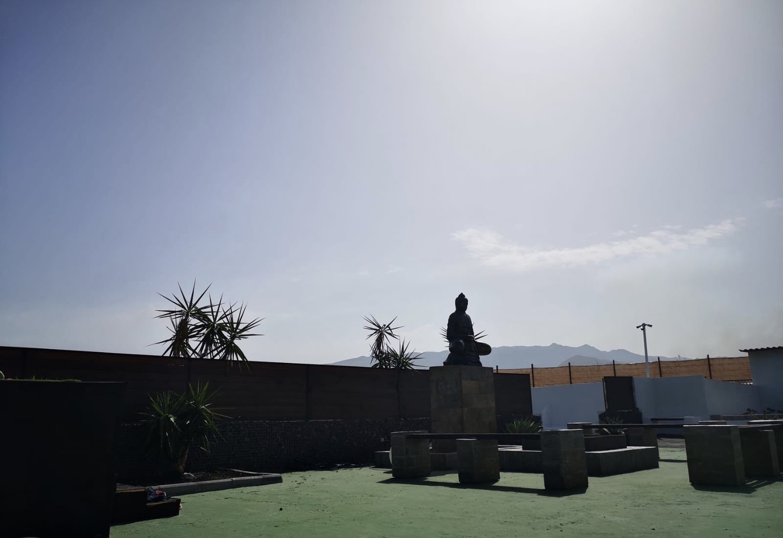 Een dakterras met een Boeddhabeeld, potplanten en uitzicht op verre bergen.